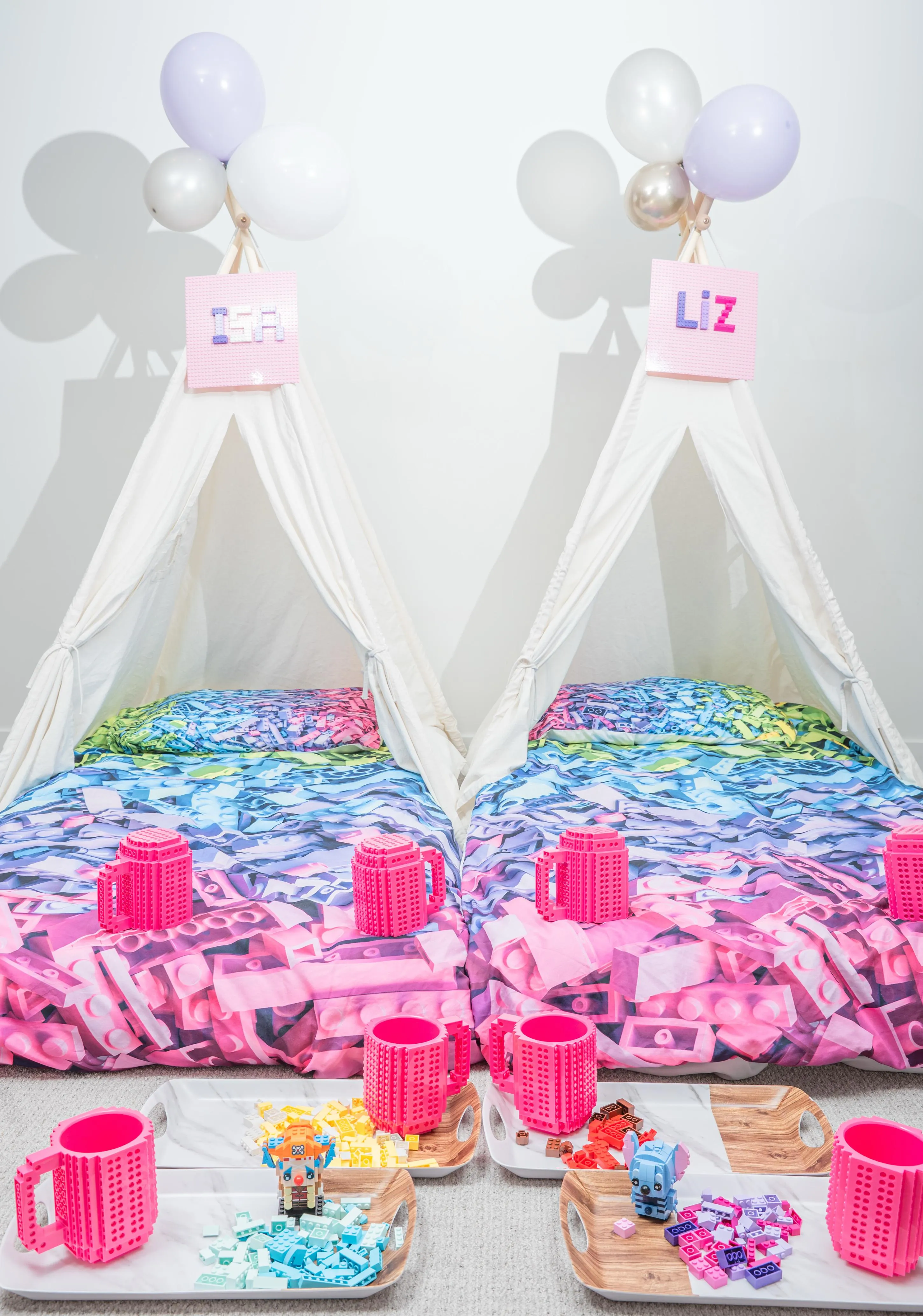 Cream sleepover tents with colourful brick-pattern bedding and pink cups.
